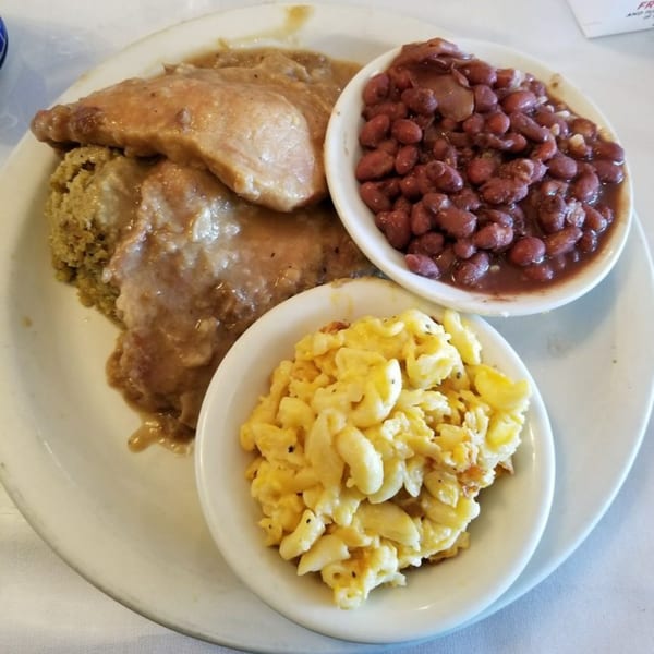 A soul food plate with gravy-covered meat and dressing, red beans, and macaroni and cheese.