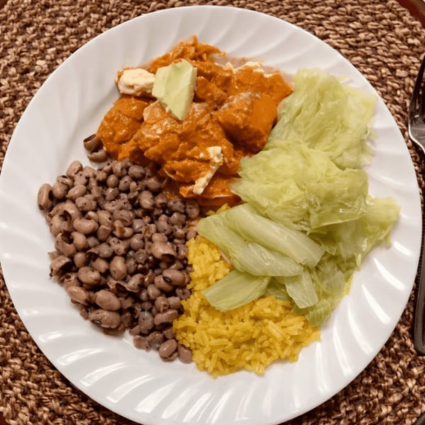A soul food plate with black-eyed peas, yellow rice, cabbage, and chicken in orange sauce.